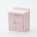 Delicate blush pink miniature kitchen cabinet featuring a protective backsplash, single drawer, and double doors with vertical grooved panels, perfect for romantic dollhouse settings.