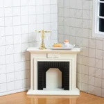 Miniature dollhouse fireplace featuring a warm ivory painted wooden mantel with simple molding details and a black insert with vertical grooved pattern interior.