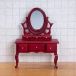 Miniature dollhouse vanity table in rich mahogany red featuring a decorative oval tilting mirror, six drawers with brass knobs, and elegant curved cabriole legs in Victorian style.