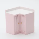 Miniature L-shaped corner cabinet in soft pink featuring double doors with vertical grooves and brass knobs, perfect for dollhouse kitchen corner storage.