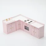 Four-piece dollhouse kitchen set in soft pink featuring an L-shaped design with sink unit, corner cabinet, stove unit with four burners, and end cabinet, all with vertical panel doors and gold hardware.