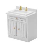 Miniature white bathroom vanity cabinet featuring a modern sink with gold-tone dual faucets, one drawer, and double doors with vertical grooves, perfect for classic dollhouse bathrooms.