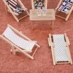 Miniature beach lounger featuring a white fabric with pink polka dots, supported by a wooden frame, perfect for dollhouse settings.