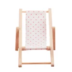 Miniature beach lounger featuring a white fabric with pink polka dots, supported by a wooden frame, perfect for dollhouse settings.