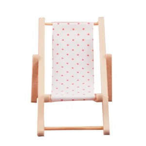 Miniature beach lounger featuring a white fabric with pink polka dots, supported by a wooden frame, perfect for dollhouse settings.