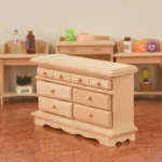 1:12 scale unfinished wooden dresser featuring eight drawers with round knobs, decorative dentil molding trim, crown top, and scalloped base for dollhouse bedroom furniture.