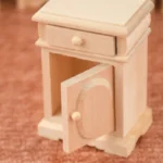 1:12 scale unfinished wooden bedside table featuring one drawer, single door cabinet with oval panel detail, scalloped base, and clean lines for dollhouse bedroom furniture.